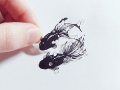 a hand holding a piece of paper with black and white designs on it, next to a drawing of a koi fish