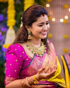 a woman in a pink and yellow sari smiles at the camera while holding her hands out