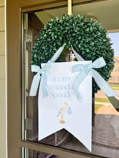 a welcome sign hanging on the front door of a house with a wreath and ribbon around it