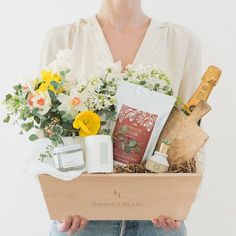 a woman holding a wooden box with flowers and personal care items in it's hands