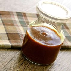 a glass jar filled with sauce sitting on top of a wooden table next to a plaid napkin