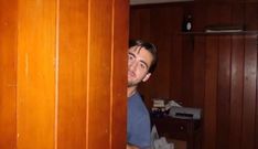 a man peeking out from behind a wooden wall in a room with wood paneling