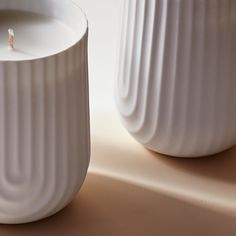 two white vases sitting next to each other on top of a table with a candle in the middle