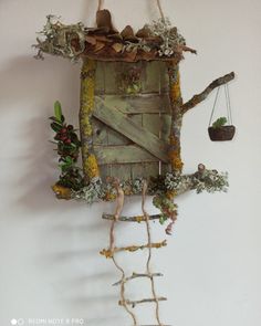 a wall hanging made out of wood and branches with plants growing on the top, along with a small potted plant next to it