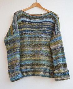 a sweater hanging on a wooden hanger next to a white wall with a blue, green and yellow striped sweater