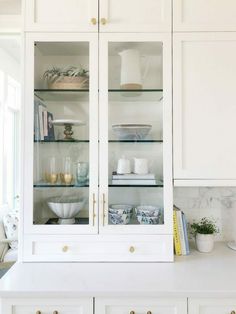 a kitchen with white cabinets and gold pulls on the glass doors, marble counter tops