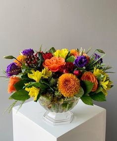 a vase filled with lots of colorful flowers on top of a white table next to a gray wall