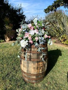 a wooden barrel with flowers and greenery in it on the grass next to trees