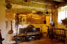 an old fashioned kitchen with pots and pans hanging from the ceiling, in front of a brick wall