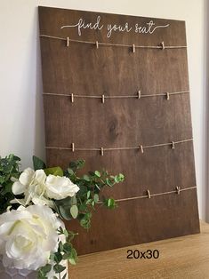 a wooden board with clothes pins attached to it next to flowers and a vase filled with white roses