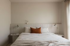 a bed with white linens and pillows in a small room next to a window