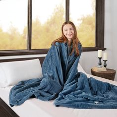 a woman wrapped in a blue blanket on top of a bed next to a window