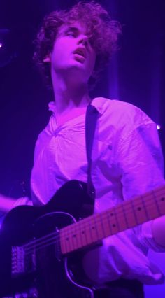 a young man with curly hair playing an electric guitar on stage at a music concert