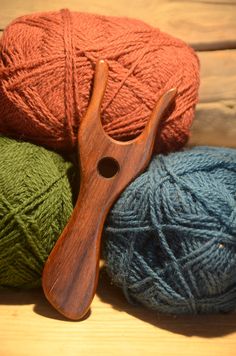 three balls of yarn and a wooden crochet hook sitting on a table next to each other