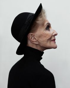 an older woman with white hair wearing a black hat and turtle - neck sweater, looking off to the side