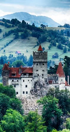 an old castle sits on top of a hill surrounded by trees and hills in the background