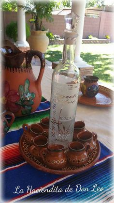 an empty bottle sitting on top of a tray next to cups and saucers in front of a window