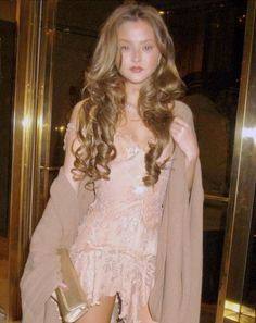 a woman is standing in front of a glass door wearing a pink dress and coat