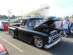 an old black truck parked in a parking lot next to other antique cars and people