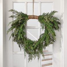 a wreath hanging on the front door of a house with pine needles and greenery