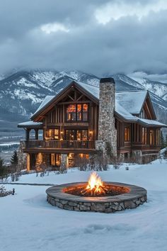 a house with a fire pit in front of it and snow covered mountains behind it