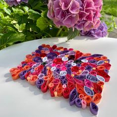 a bunch of colorful paper flowers sitting on top of a white table next to purple and pink flowers