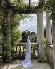 a woman in a white dress is standing on a porch with columns and ivys