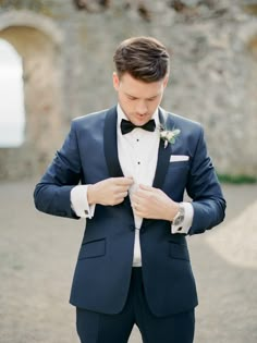 a man in a tuxedo adjusts his bow tie