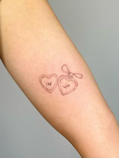 a woman's arm with two hearts and a bow tattoo on the left forearm