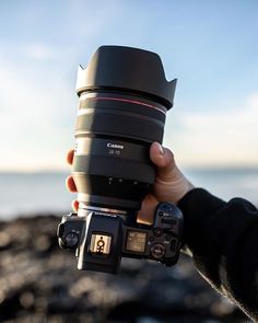 a person holding up a camera in front of the ocean