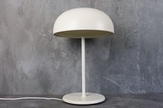 a white table lamp sitting on top of a cement floor next to a gray wall