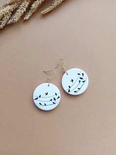 the earrings are made from white and black paper with birds on it, sitting next to some dried grass