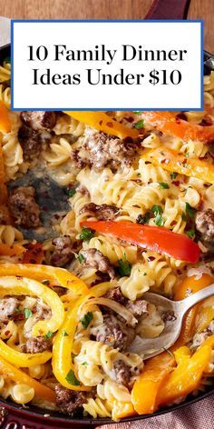 a skillet filled with pasta and vegetables on top of a wooden table next to a spoon