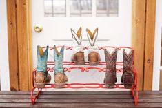 several pairs of cowboy boots are on a red shoe rack in front of a white door