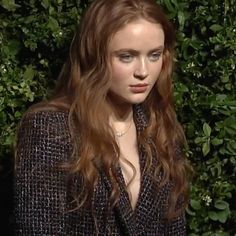 a woman with long hair standing in front of bushes