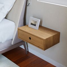 a small wooden table with a photo frame on it next to a bed and pillows