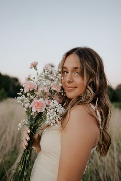 a woman in a white dress is holding some pink and white flowers on her shoulder