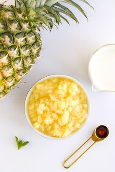 a pineapple next to a bowl of oatmeal and spoons on a white surface