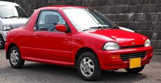 a small red car parked in front of a brick wall next to another white car