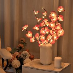 an arrangement of flowers in a white vase on a table next to a lit candle