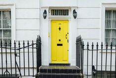 a yellow door is on the front of a white house with black iron fence and gate