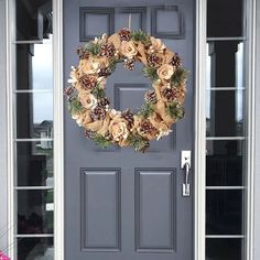 a wreath on the front door of a house with pine cones and flowers hanging from it