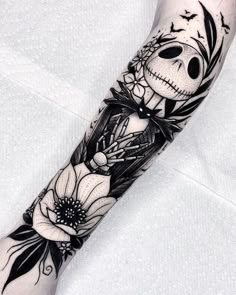 a black and white tattoo with flowers on the arm, skull in center surrounded by birds