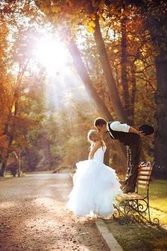 a bride and groom kissing on a bench in the middle of an autumn park setting