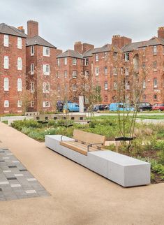 a bench sitting in the middle of a park next to tall brick buildings and green grass