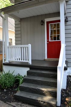 a red door is on the side of a gray house with steps leading up to it