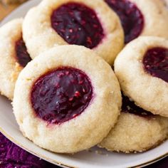 several cookies with jelly on them are sitting on a plate next to some purple cranberry sauce