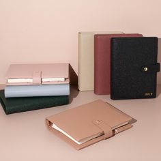 three different colored notebooks sitting next to each other on top of a table in front of a pink wall