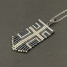 a black and white beaded necklace on a silver chain with a square pendant hanging from it