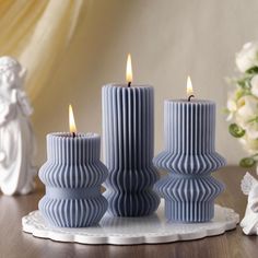 three blue candles sitting on top of a table next to white angel figurines